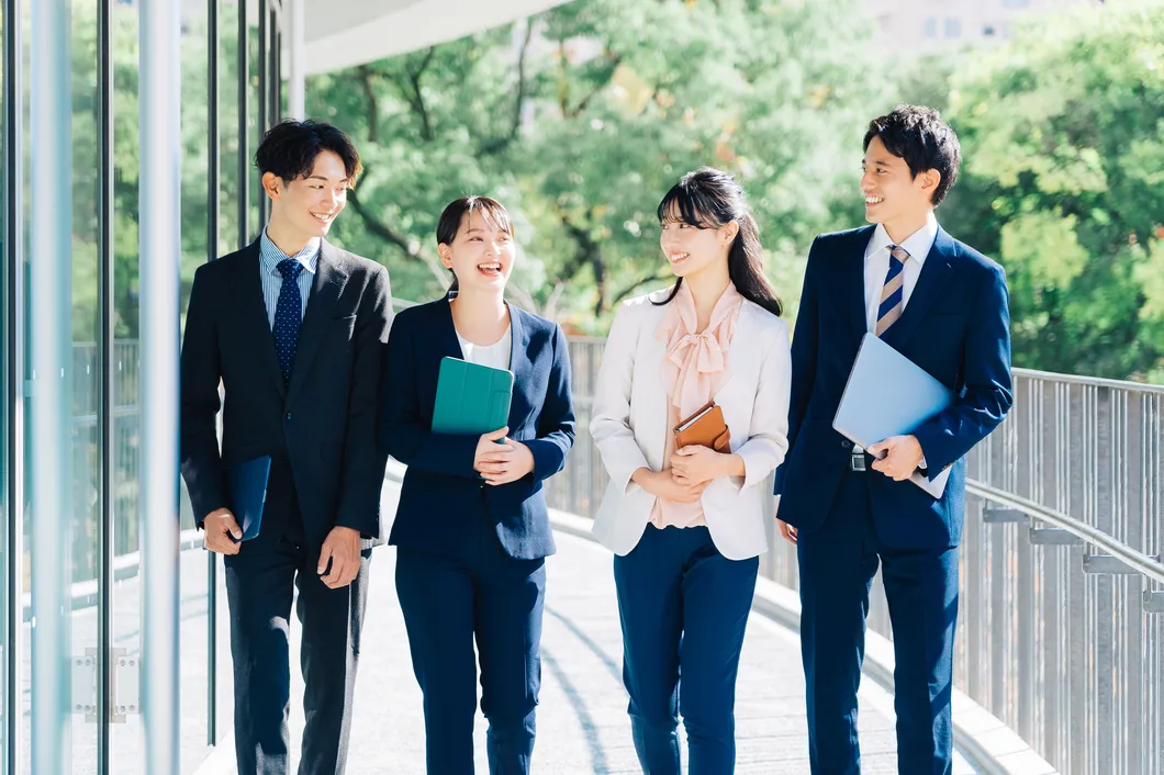 屋外を歩きながら笑顔で会話するスーツ姿の若手ビジネスパーソン