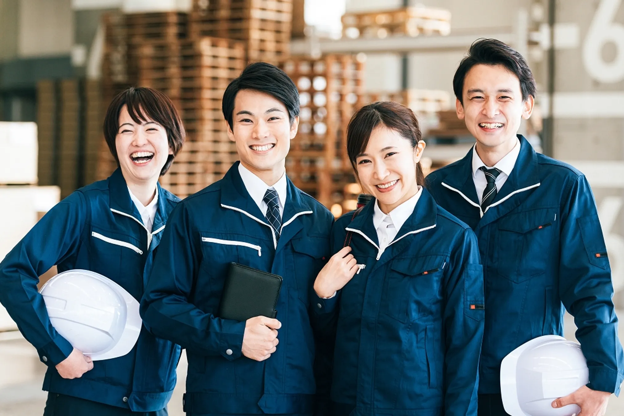 作業服を着用した4人の男女が、笑顔で正面を向いている写真