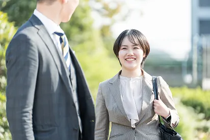 グレーのスーツを着た女性が、スーツ姿の男性を笑顔で見ている様子