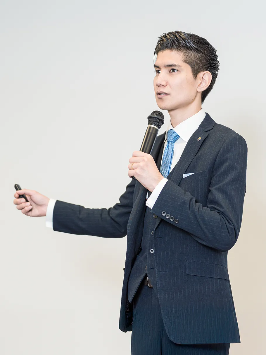 スーツを着た男性がマイクを持って話をしている様子