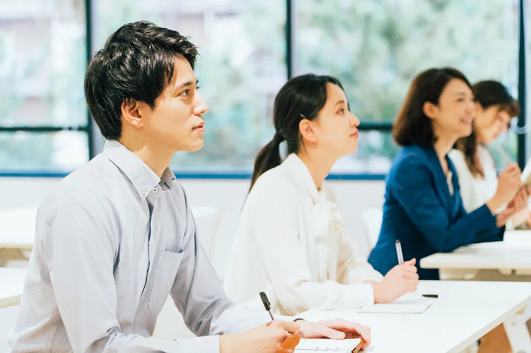 若手の男女社員が横並びに座り、真剣な表情で前方の講義に耳を傾けている写真