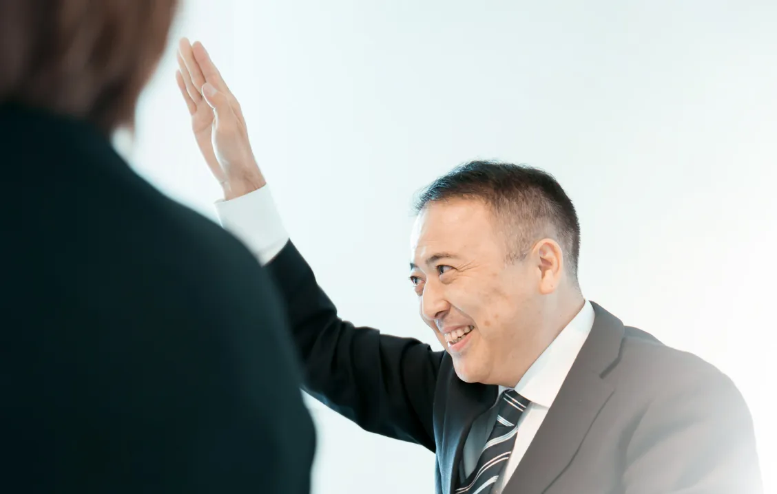 スーツ姿の男性が笑顔で手を挙げ、対話をしている写真
