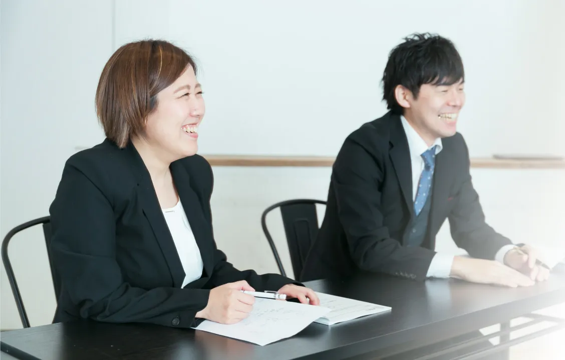 会議中にスーツ姿の女性と男性が笑顔で会話している写真
