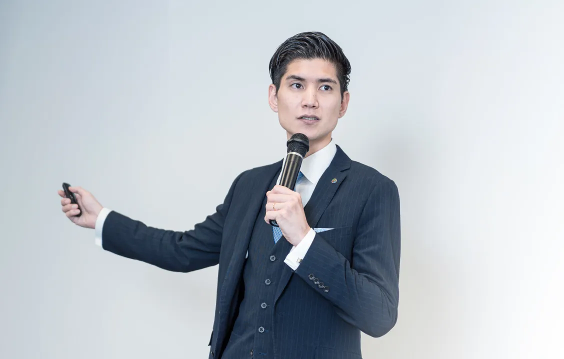 マイクを持ったスーツ姿の男性が真剣な表情で話をしている写真