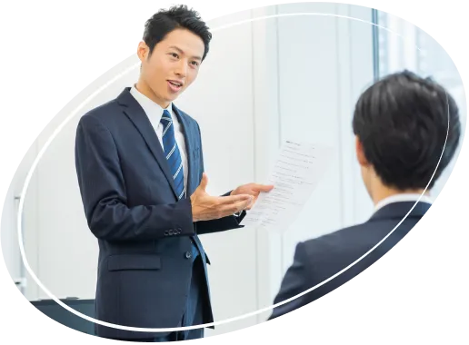 書類を手に持ち、後ろ姿の男性に向かって話をしているスーツ姿の男性