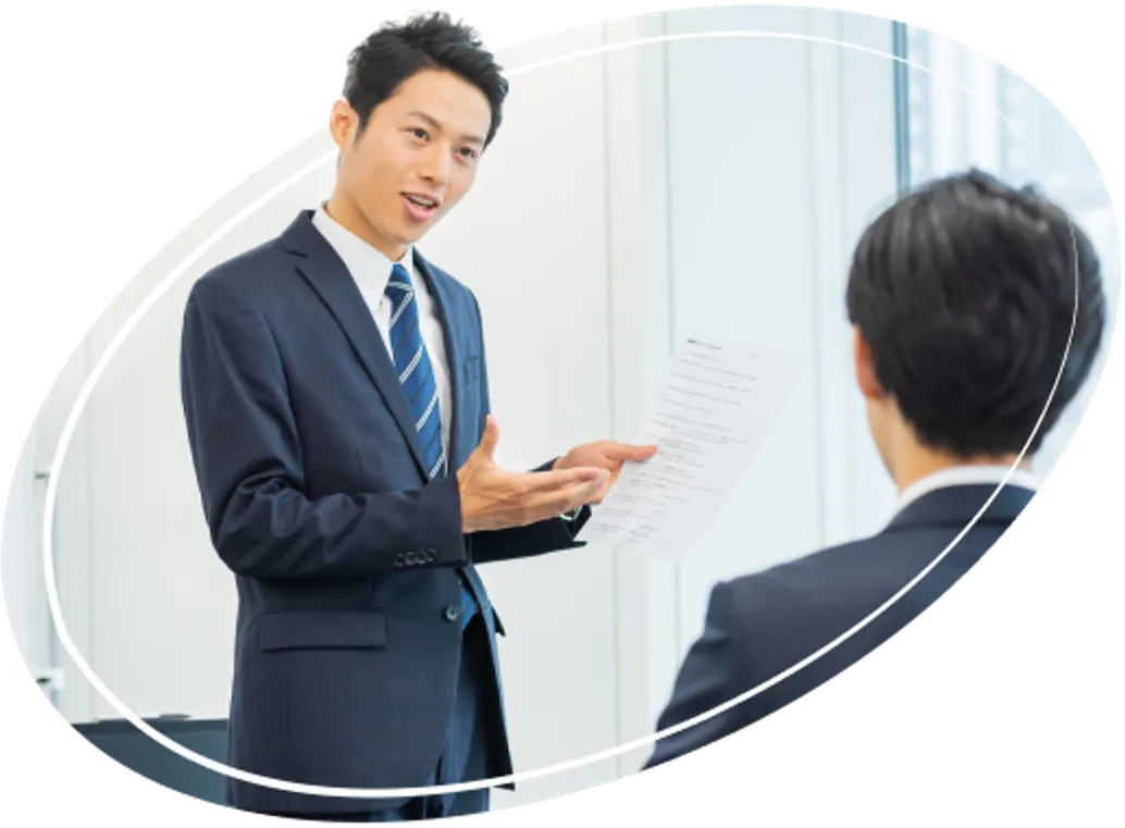 書類を手に持ち、後ろ姿の男性に向かって話をしているスーツ姿の男性