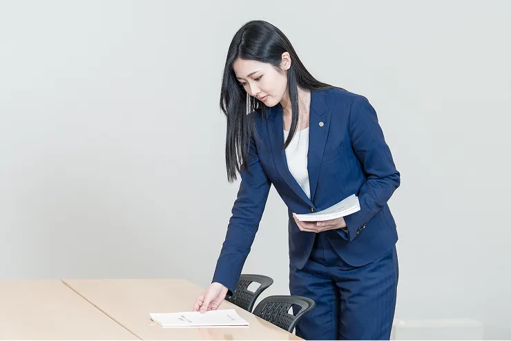スーツを着た女性社員が会議室のテーブルに資料を並べて準備をする様子