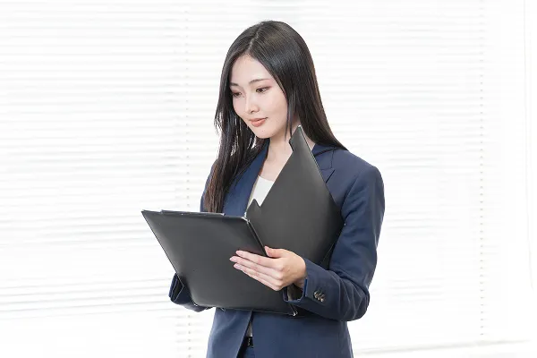 スーツ姿の女性がバインダーを手に持ち、資料を確認する様子