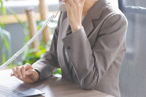 グレーのスーツを着た女性社員が、電話で会話しつつパソコンを操作する様子